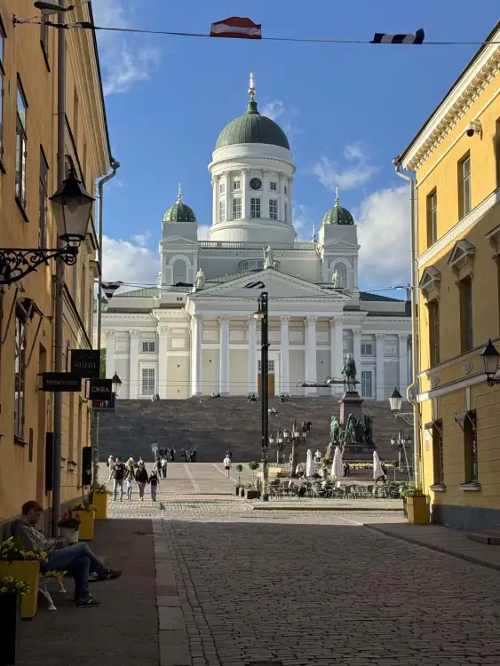 Evening view of Helsinki Cathedral and Senate Square from Sofiankatu, a cobblestone street lined with old buildings.