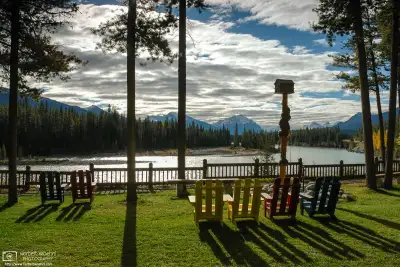 At a lodging facility in Jasper National Park, Alberta, colorful deck chairs are facing a bend of the Athabasca River. Mount Kerkeslin is visible in the distance.