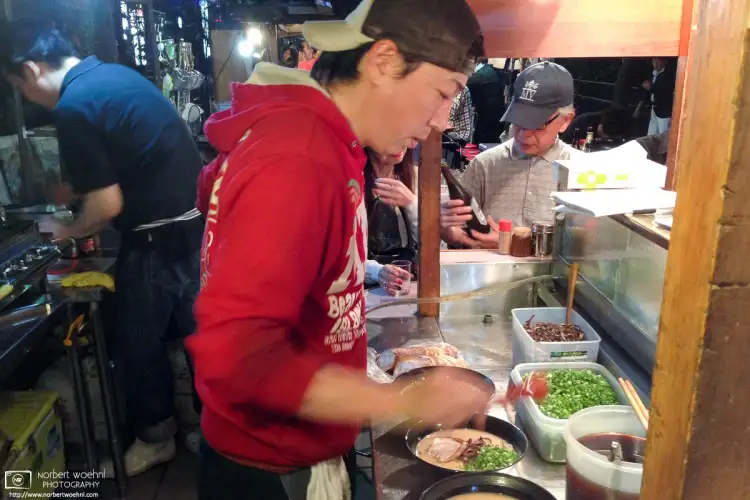 Staff preparing servings of Hakata Ramen noodles inside a typical Yatai food stall in Fukuoka, Japan.