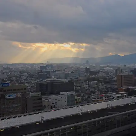 Rays of sunlight are breaking through the clouds to illuminate the southern part of central Kyoto. The pagoda of Toji Temple is visible towards the right side.