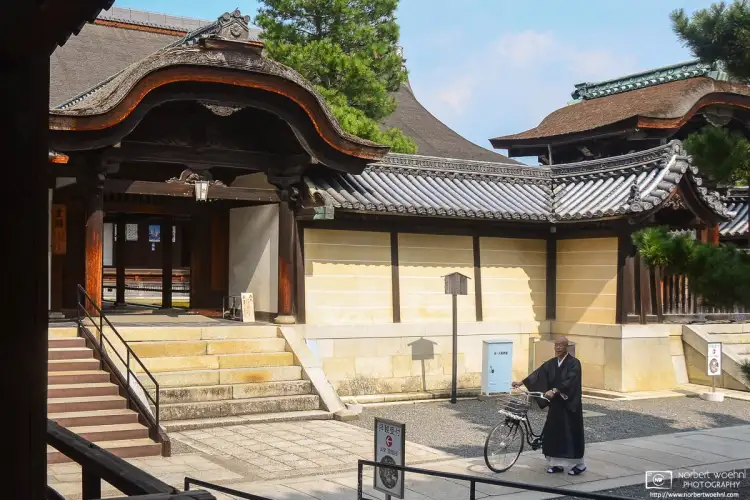 A priest is pushing his bicycle across the premises of Myōshinji Temple in Kyoto, Japan.