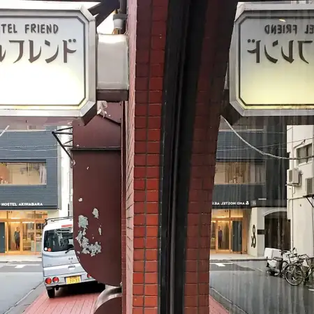 In the Taito Ward of Tokyo, Japan, a Showa-era hotel sign is reflected in a window, opening up a view towards a quiet backstreet with a more contemporary hotel.