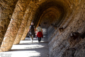 Visitors are seen walking down a colonnaded pathway at Antoni Gaudí's Parc Güell in Barcelona, Spain.