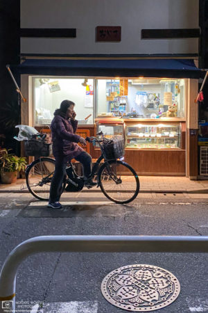 A woman is seen making a phone call in front of an old-style neighborhood shop in Itabashi-ku, Tokyo, Japan.