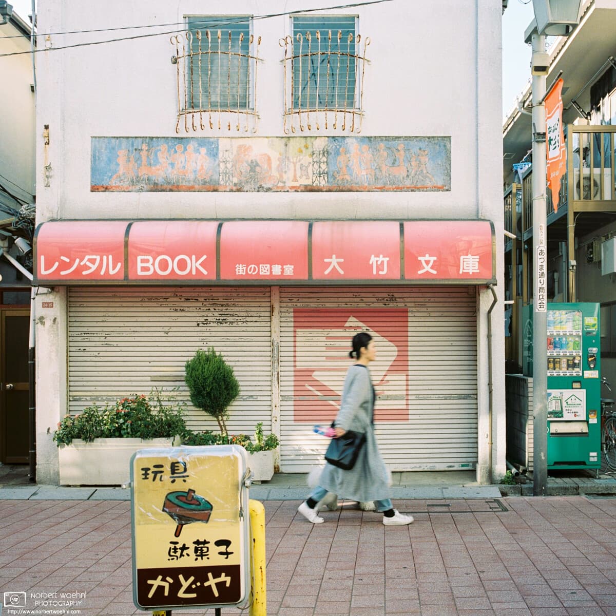 A woman walks past the slightly dated facade of a rental book store in Koenji, Tokyo, Japan.